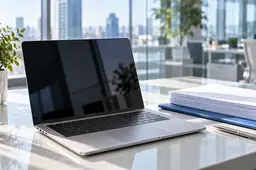 Zilveren laptop naast een stapel witte documenten, een blauwe map en een pen op een licht kantoorbureau