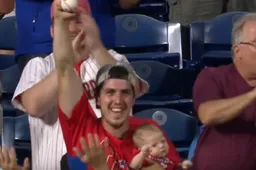 Bazige vader vangt bal tijdens honkbalwedstrijd terwijl hij zijn baby vasthoudt