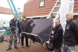 Twee mannen met een zonnepaneel bij een woning.