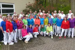 Leden van musical- en popkoor Ermelodie poseren buiten in kleurrijke kleding.
