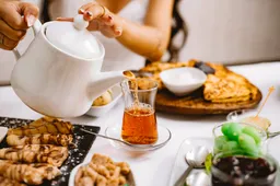 woman-pouring-black-tea-from-white-ceramic-teapot-into-armudu-glass-side-view