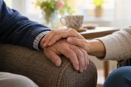 Twee mensen houden elkaars hand vast in een huiselijke omgeving.