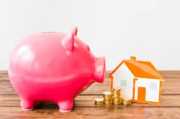 pink-piggybank-near-stacked-coins-house-wooden-desk