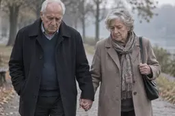 Ouder echtpaar loopt hand in hand over een herfstig pad langs het water