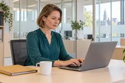 Vrouw aan een bureau in een kantoor typt een e-mail op haar laptop
