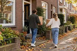 Jong stel draagt verhuisdozen naar de voordeur van een bakstenen rijtjeshuis in de herfst