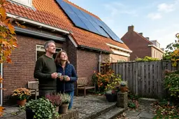 Nederlands stel met koffiemokken kijkt in de achtertuin omhoog naar zonnepanelen op het rode pannendak van hun woning.