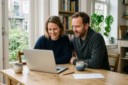 Stel aan een houten keukentafel met een geopende laptop, een witte envelop, een balpen en twee koffiemokken.
