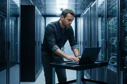IT-beheerder in een serverruimte kijkt geconcentreerd naar een laptop op een karretje tussen rekken met lampjes.