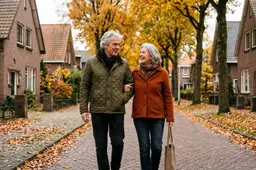 Een Nederlands echtpaar van begin zestig wandelt in de herfst langs een rij bakstenen woningen.