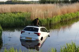 Auto belandt in sloot, bestuurder kruipt dak op
