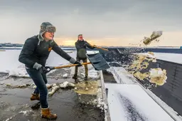 Broers Fons (62) en Kees (60) van Okido Heerenveen vegen snel de sneeuw van hun platte dak. ‘Je weet maar nooit’