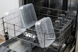 Plastic bakjes vol waterdruppels in het bovenrek van een open vaatwasser.