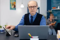 Een man van rond de zeventig werkt achter een bureau op een kantoor.