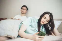 Een man en een vrouw liggen 's avonds in bed en kijken op hun telefoon.