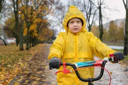 Portret van serieuze kleuter in gele regenjas. Jongen fietst in een herfstpark in de regen