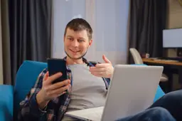 Een man zit ’s avonds alleen op de bank en chat op zijn telefoon.