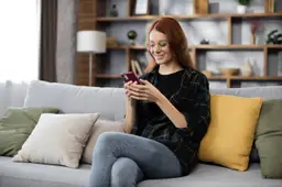 Een vrouw zit op de bank en typt op haar telefoon een tekst voor haar datingprofiel.