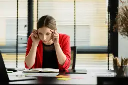 Een vrouw zit aan haar bureau en kijkt met haar hoofd in haar hand naar een kalender.