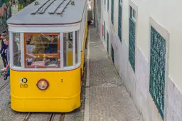 Een gele tram rijdt door een smal, steil straatje in de oude wijk Alfama in Lissabon.