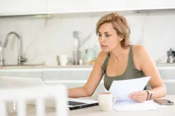 Een vrouw van rond de veertig bekijkt aan de keukentafel haar pensioenoverzicht op een laptop.