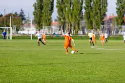 Amateurvoetballers strijden om de bal op een kunstgrasveld van een dorpsclub.