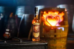 Een fles Compass Box Flaming heart 2025 25th Anniversary Edition whisky met op de achtergrond een brandend vat met een hart erin