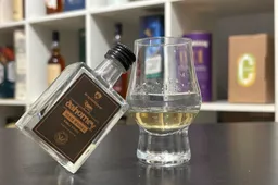 dahomey peated grain fles op een tafel met een glas whisky waar de fles tegenaan leunt