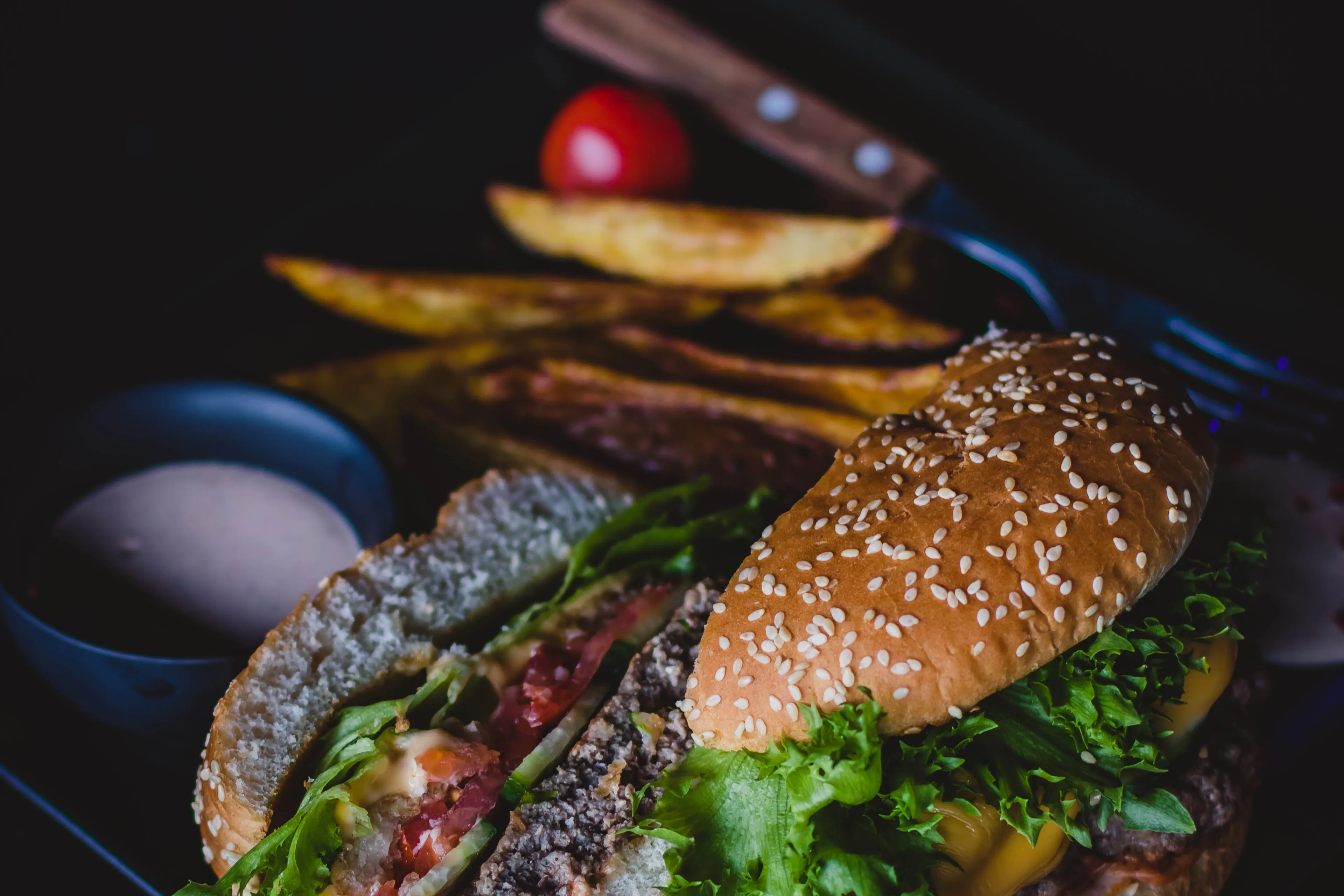 canva burger with green leafy vegetable and cheese on black plate