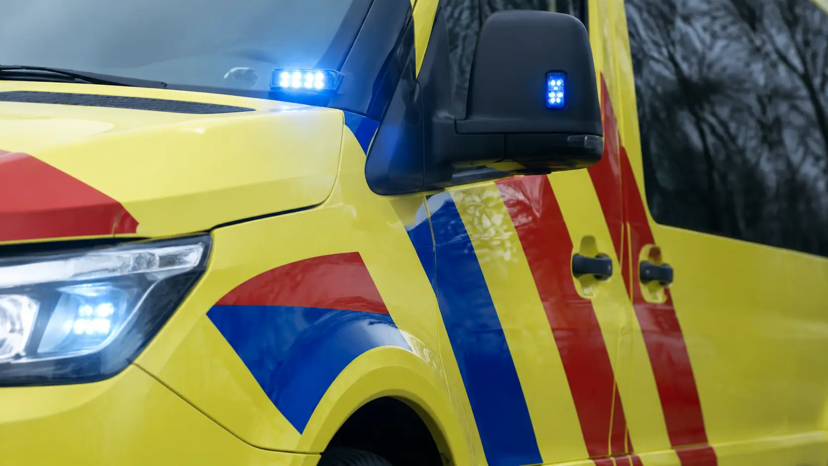 Detail van een gele ambulance met rood-blauwe strepen en blauwe zwaailichten