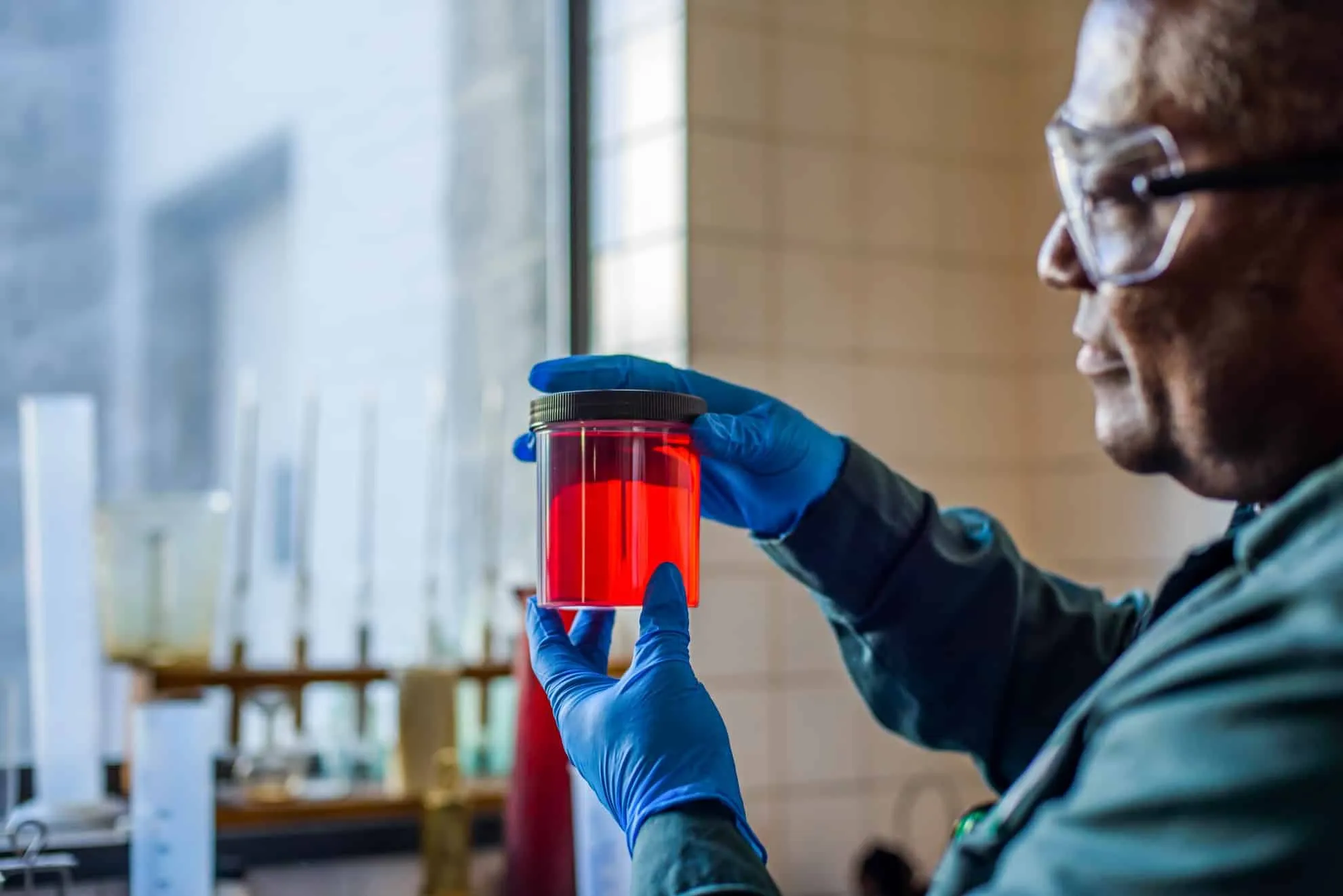 lab technician looking at beaker of red biofuel in 2022 03 04 01 54 40 utc