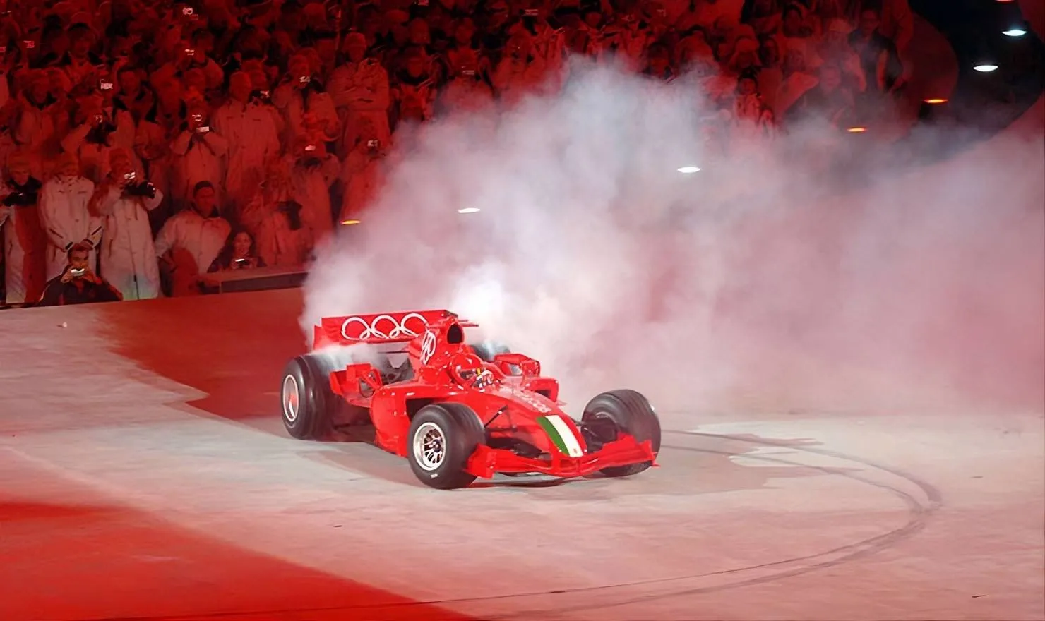 Luca Badoer sulla Ferrari F2005 esegue dei tondi tra il fumo delle gomme durante la cerimonia di apertura delle Olimpiadi invernali di Torino 2006, con i cerchi olimpici ben visibili sull'alettone posteriore