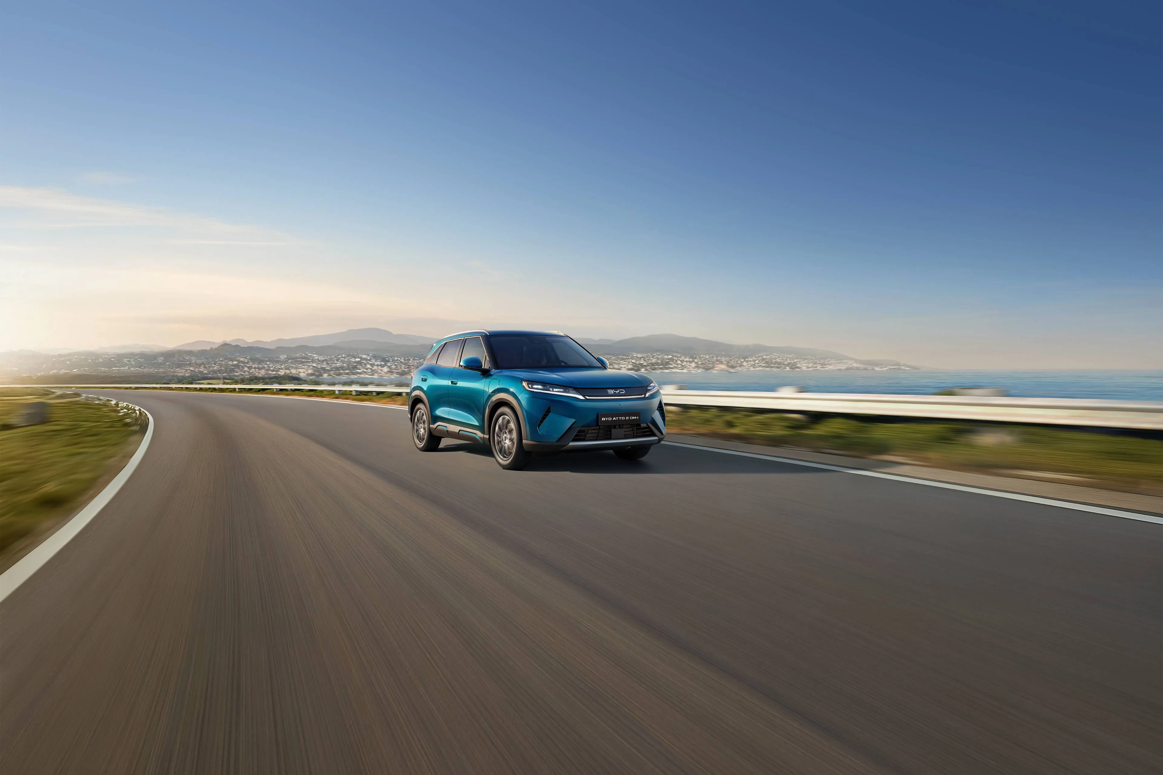 Nell'immagine si vede la BYD ATTO 2 DM-i su strada con uno sfondo costiero