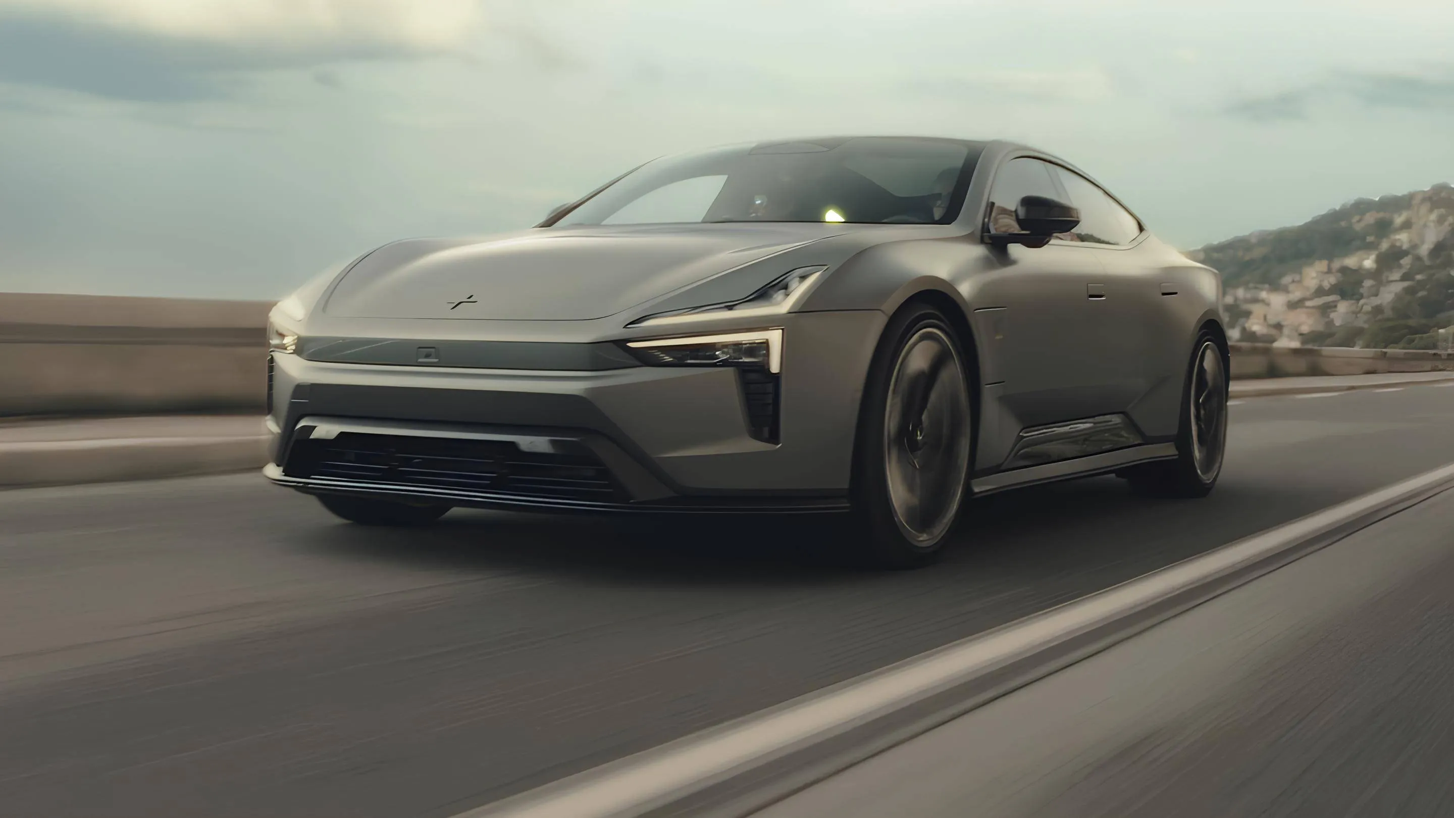Nell'immagine si vede la Polestar 5 grigia che percorre una strada e sullo sfondo si vede una collina