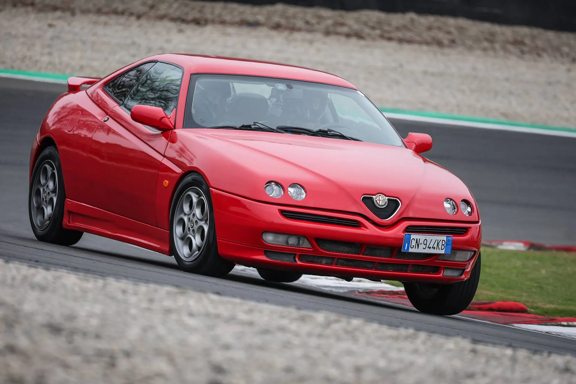 alfa romeo gtv di colore rosso che percorre una curva in pista