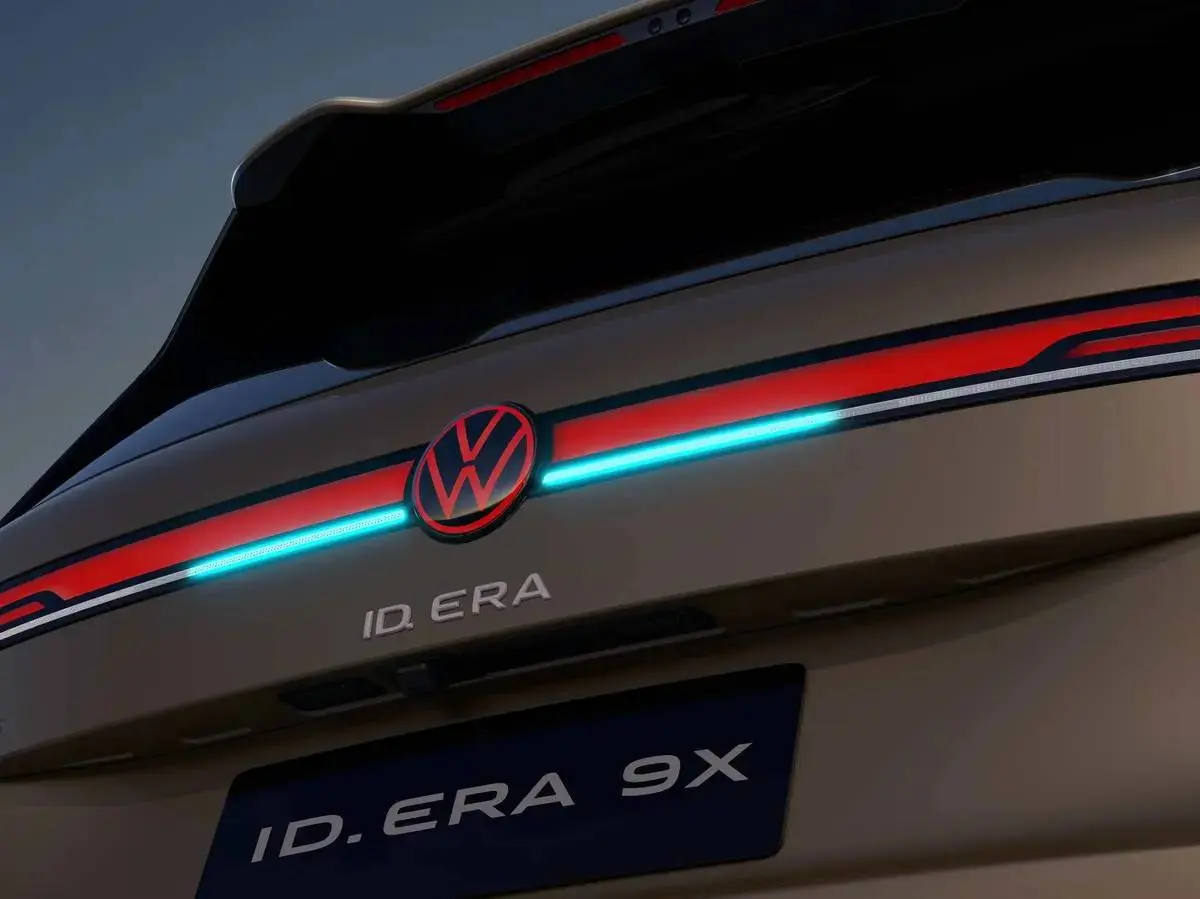 Dettaglio posteriore del SUV Volkswagen ID. Era 9X color bronzo. Spicca la firma luminosa a tutta larghezza con barra LED bicolore rossa e azzurra, divisa al centro dal logo VW illuminato di rosso. Sotto, il lettering ID. ERA