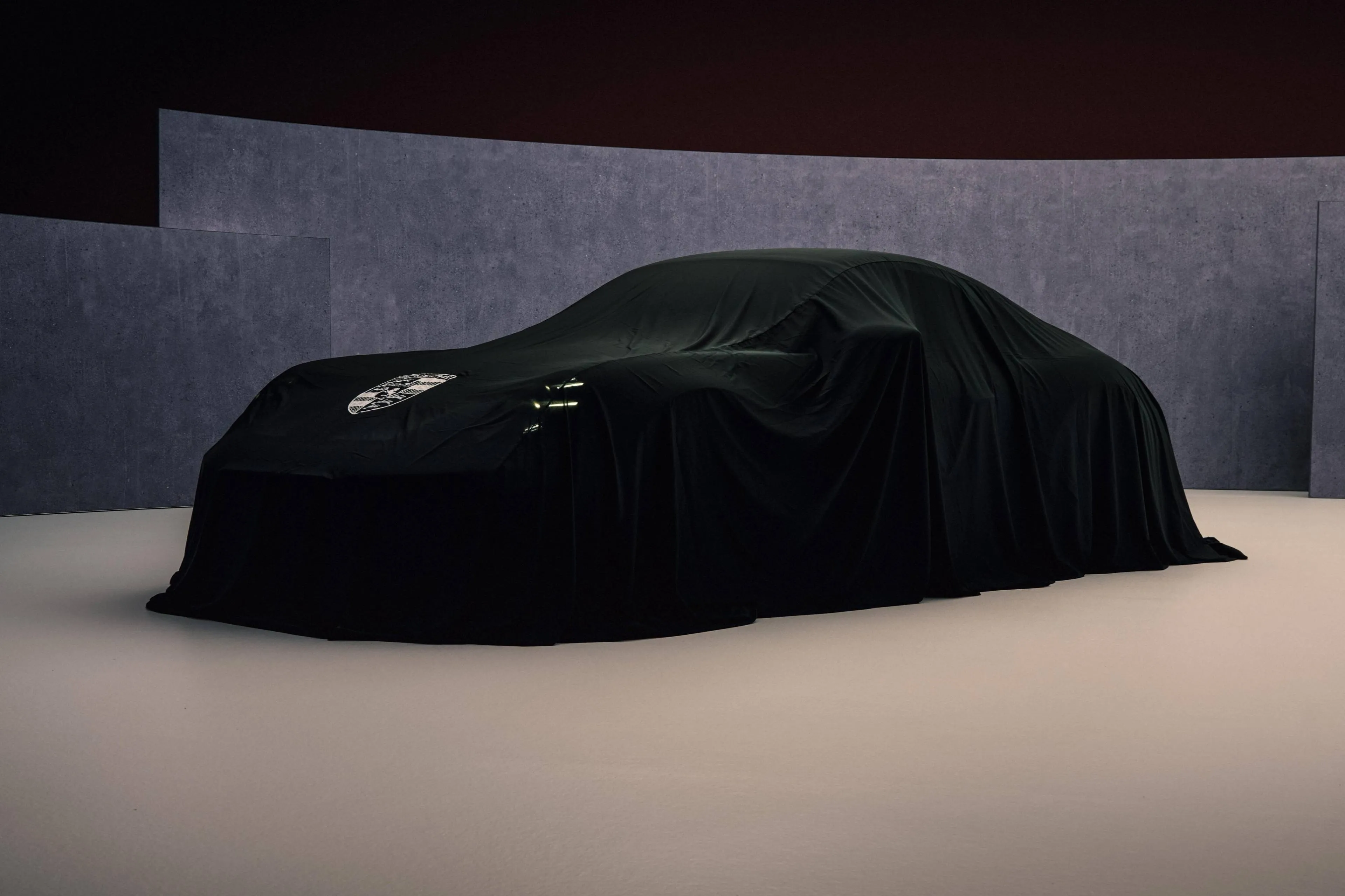 nuova porsche 911 coperta da un telo nero con sfondo grigio e pavimento beige