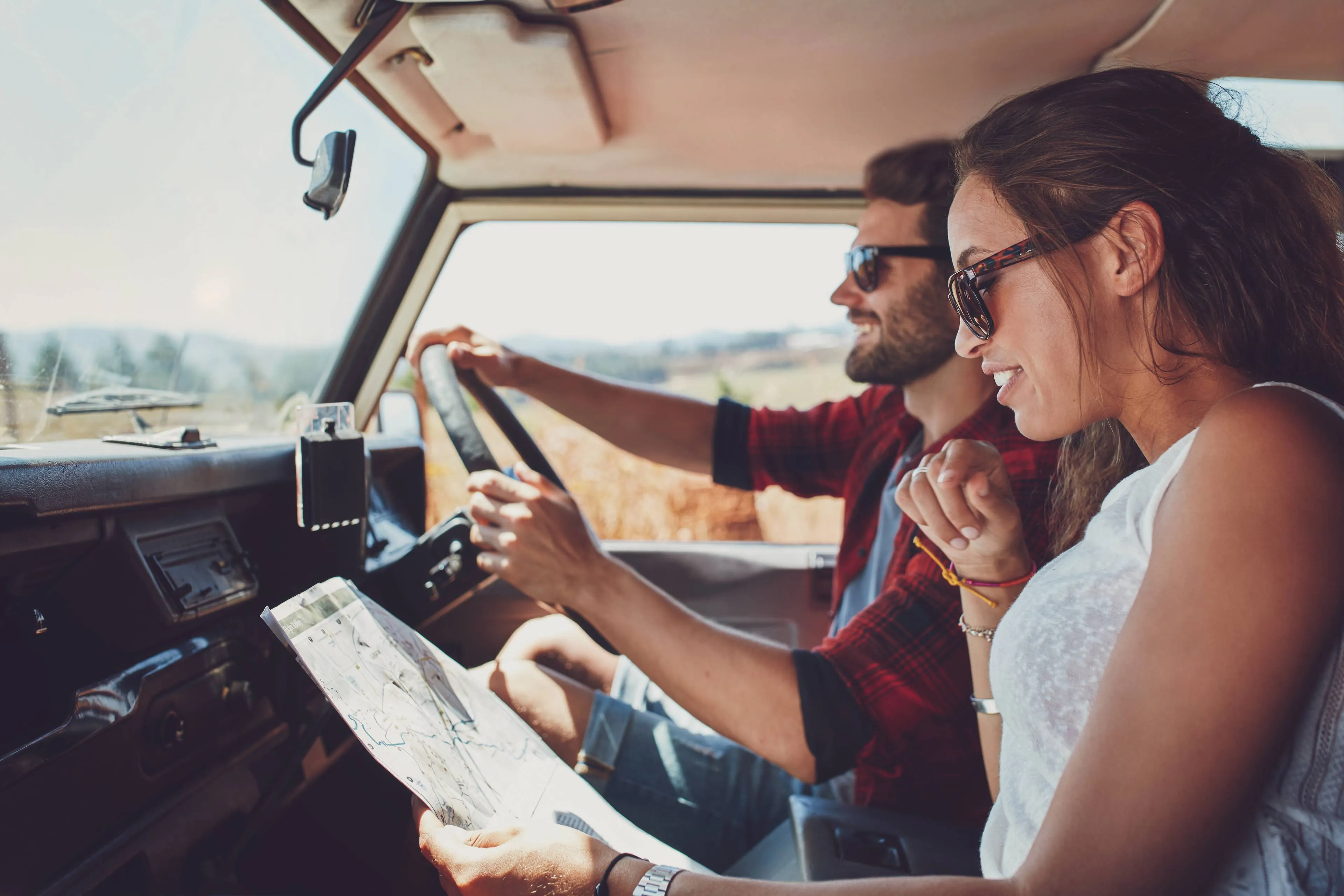 due persone su un'auto che guardano la mappa e il cellulare mentre partono per un viaggio
