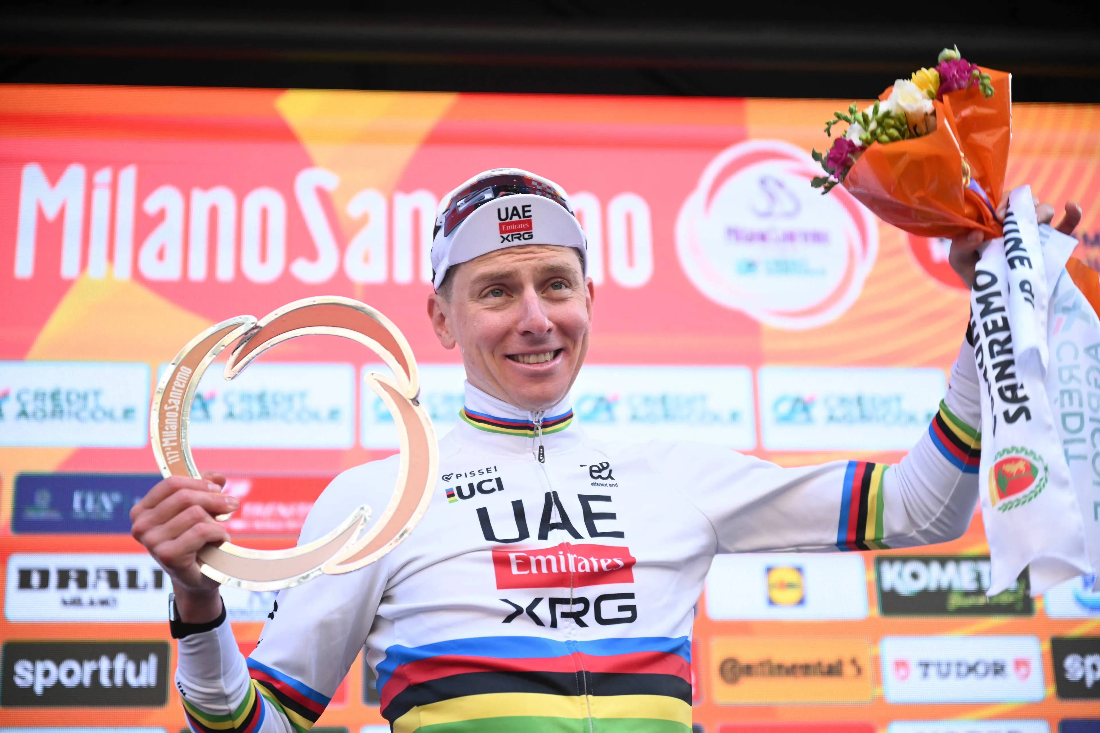 Tadej Pogacar holds aloft the trophy and a bunch of flowers after winning Milano-Sanremo 2026