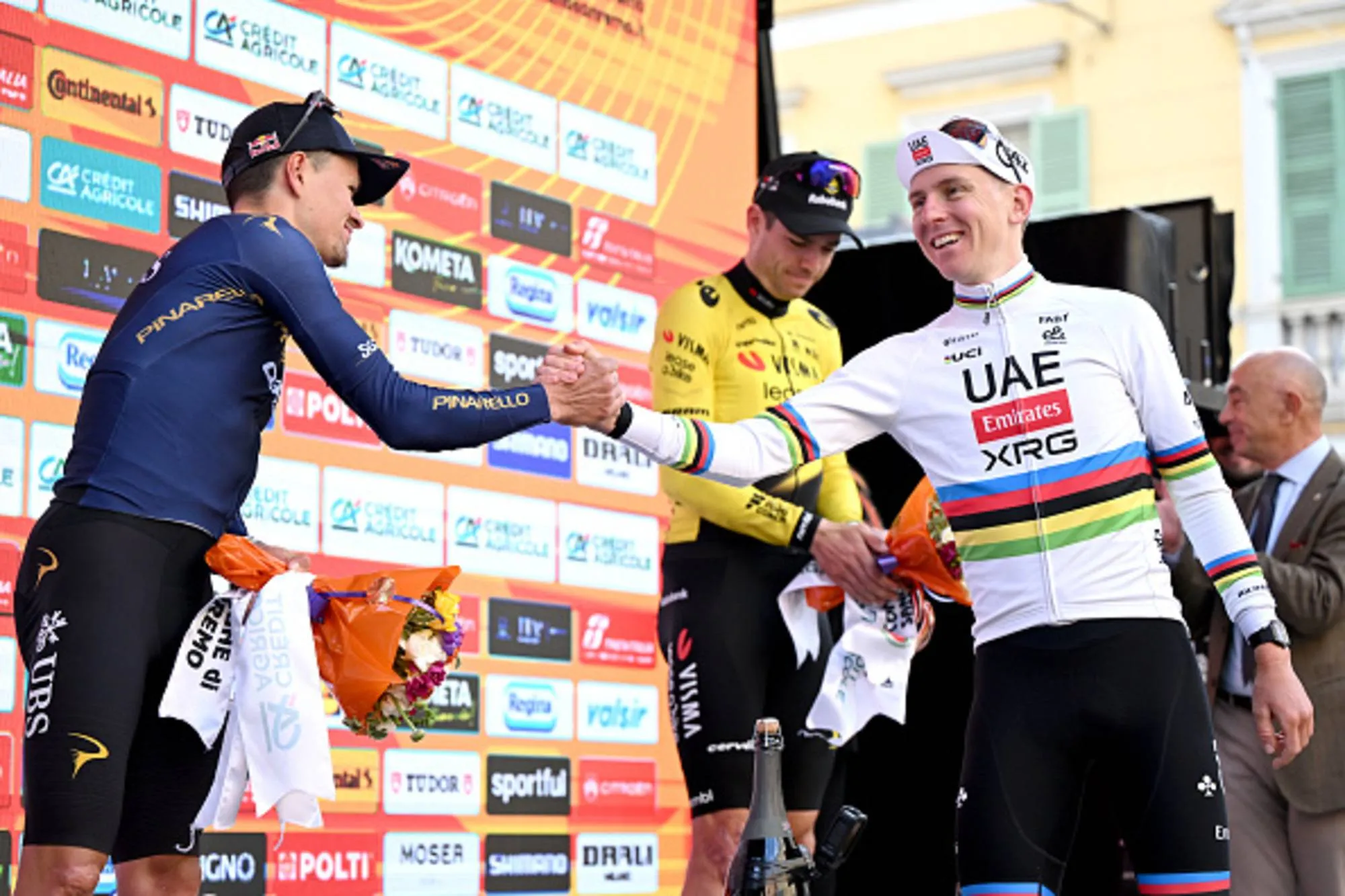 Tadej Pogacar and Tom Pidcock shake hands on the final podium of Milano-Sanremo 2026 whilst Wout van Aert watches on