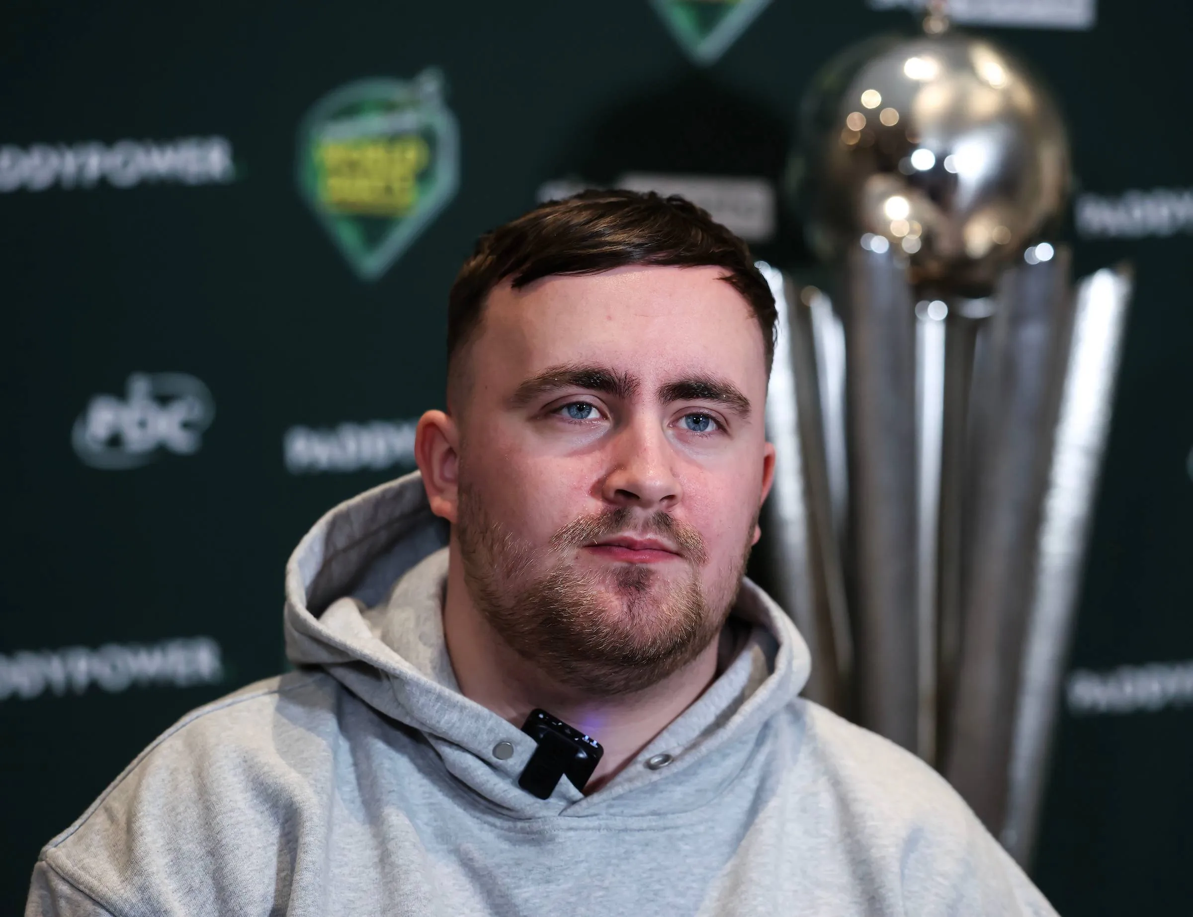 Luke Littler poses with the Sid Waddell Trophy looming large in the background