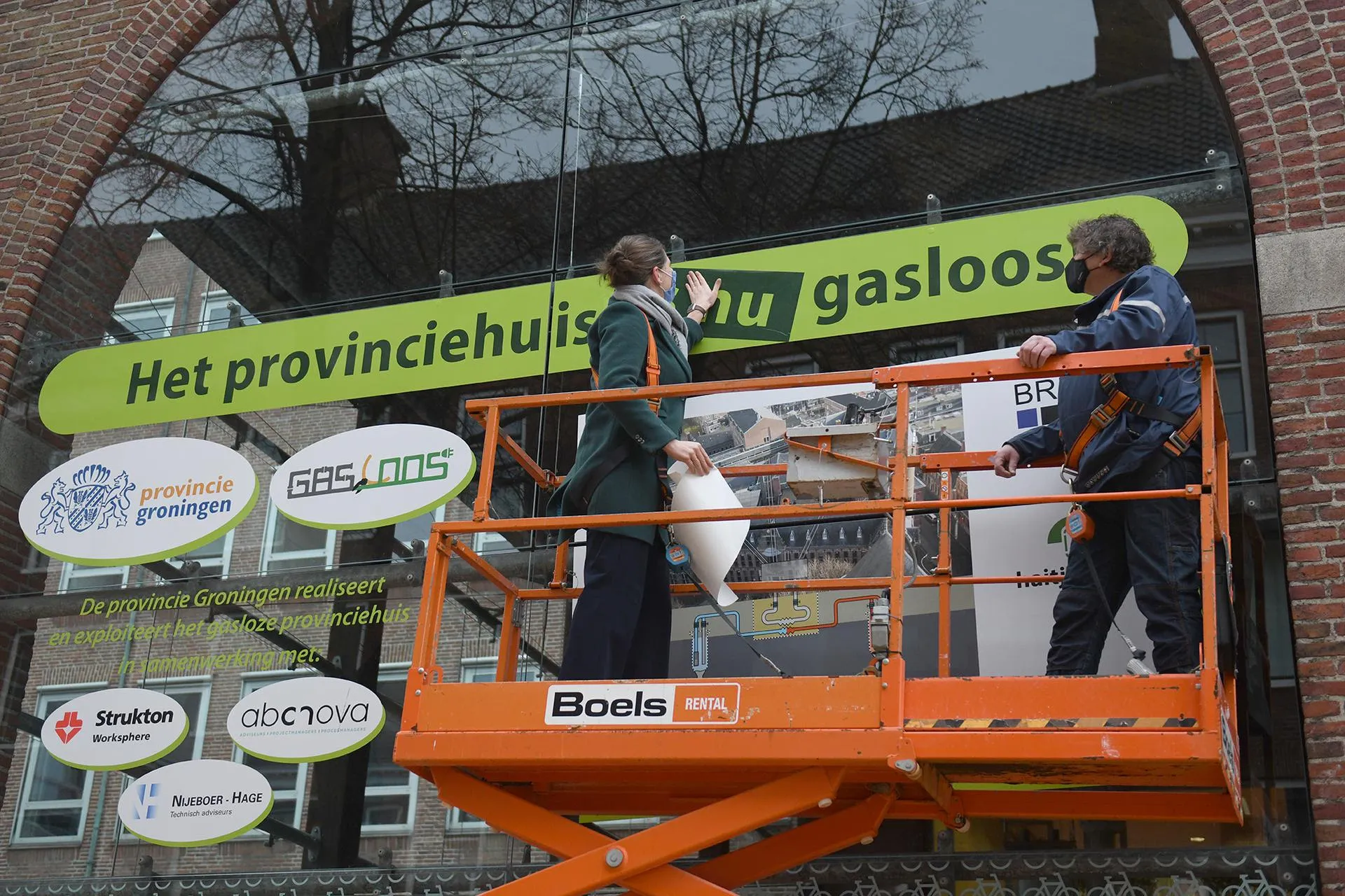 gedeputeerde fleur graper van koolwijk plakt de sticker het provinciehuis is nu gasloos op een bouwbord