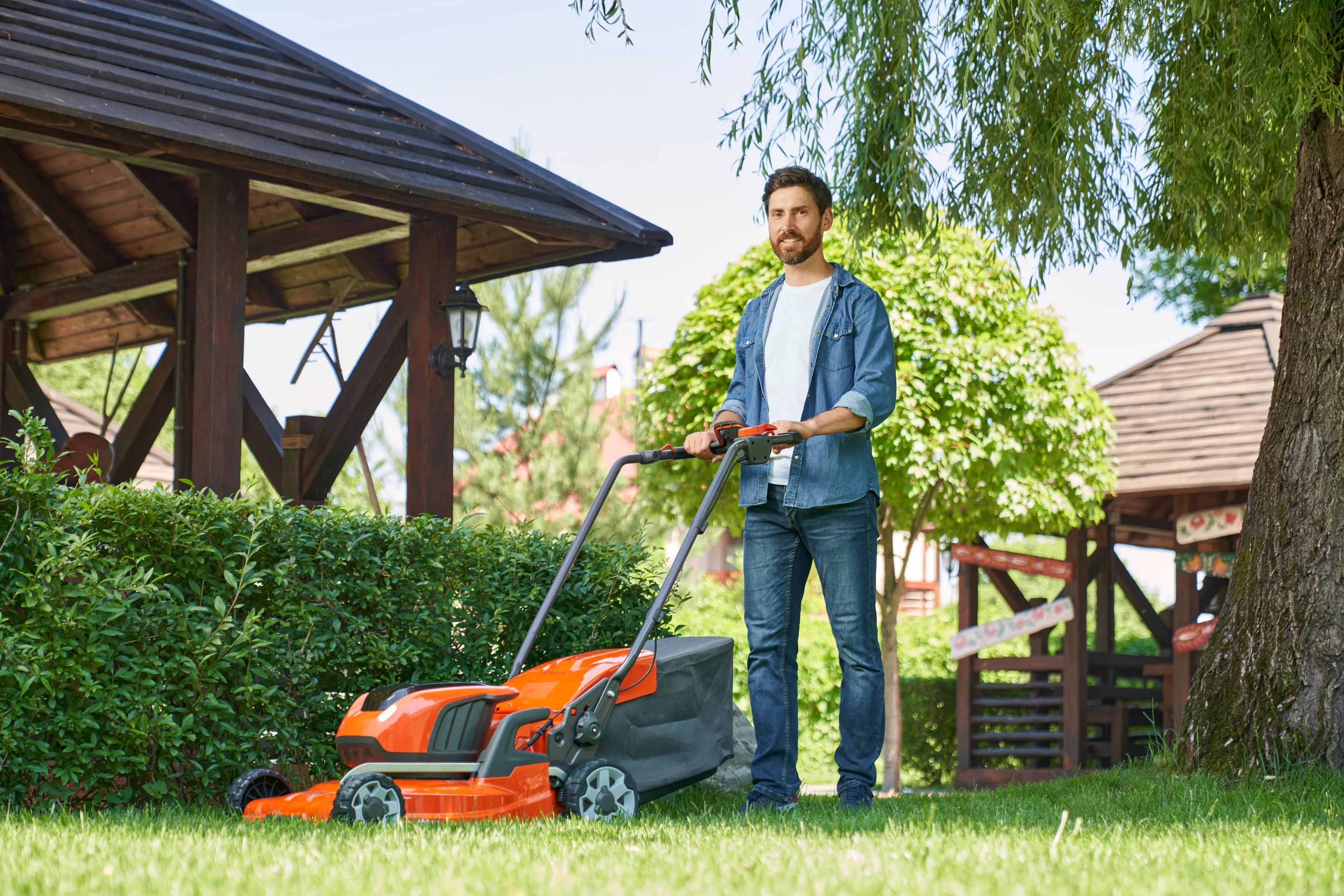 smiling-male-landscaper-denim-shirt-trimming-overgrown-lawn-with-lawn-mover-summer-day-low