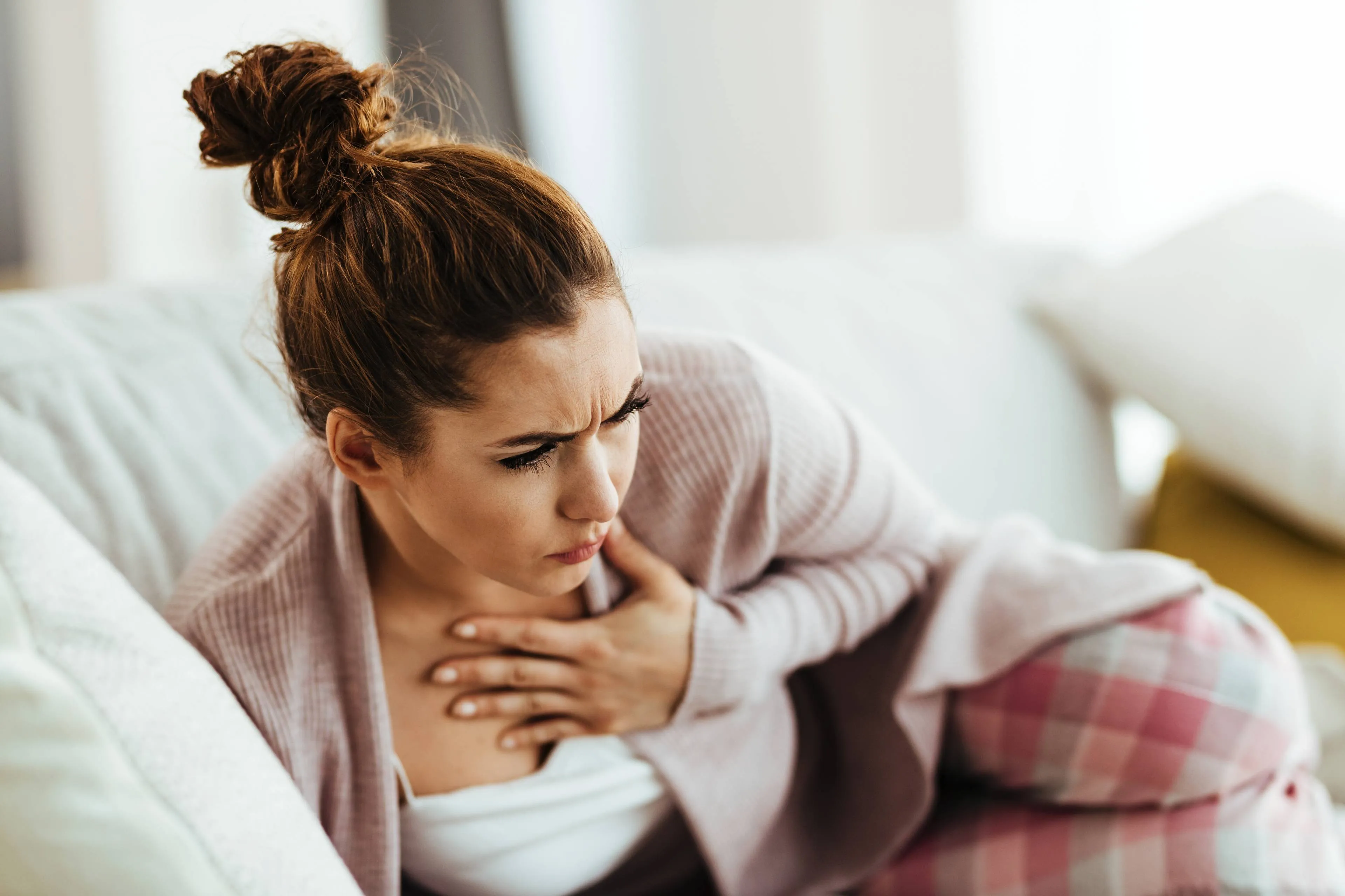 distraught-woman-holding-her-chest-pain-while-lying-down-sofa-living-room