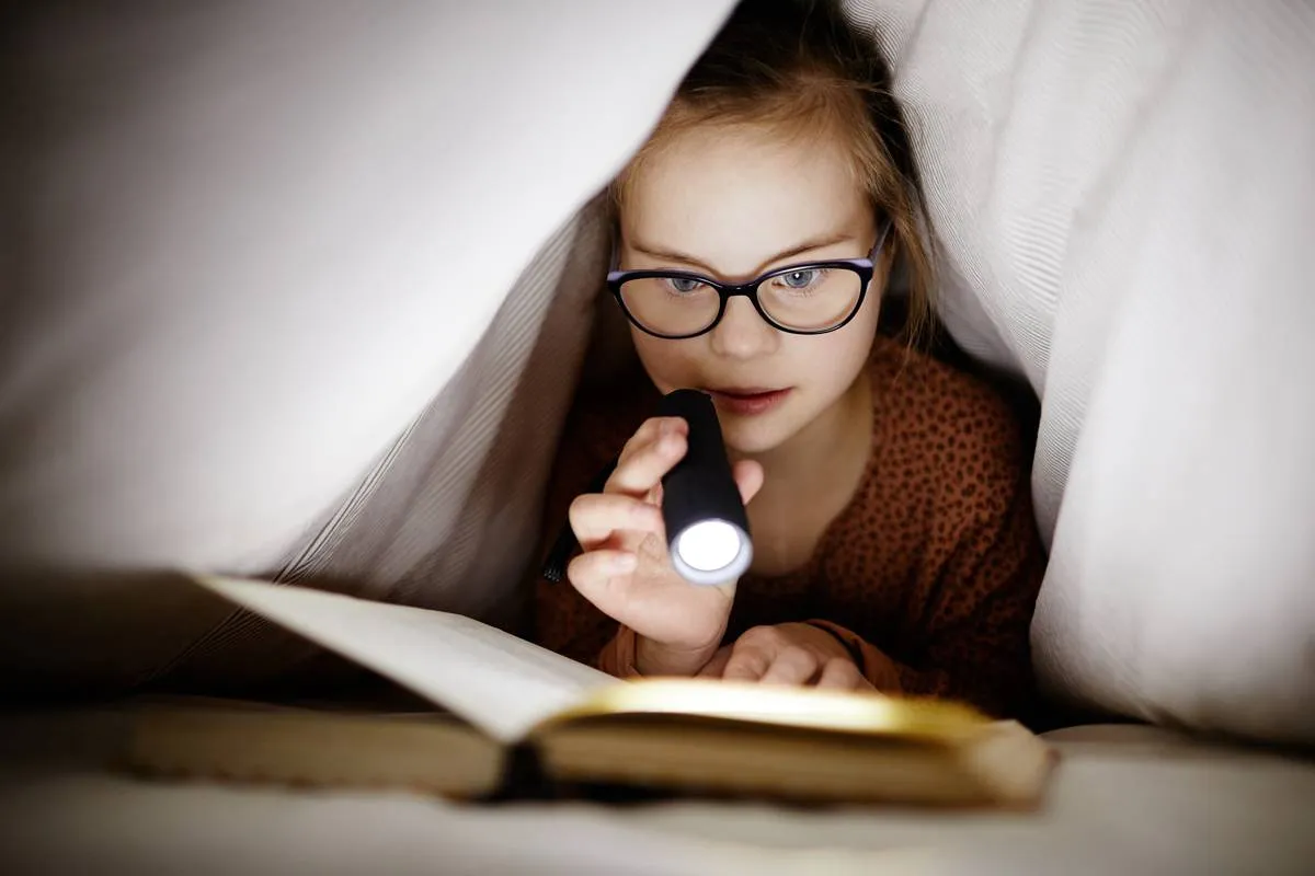 kind leest boek onder de dekens met zaklamp
