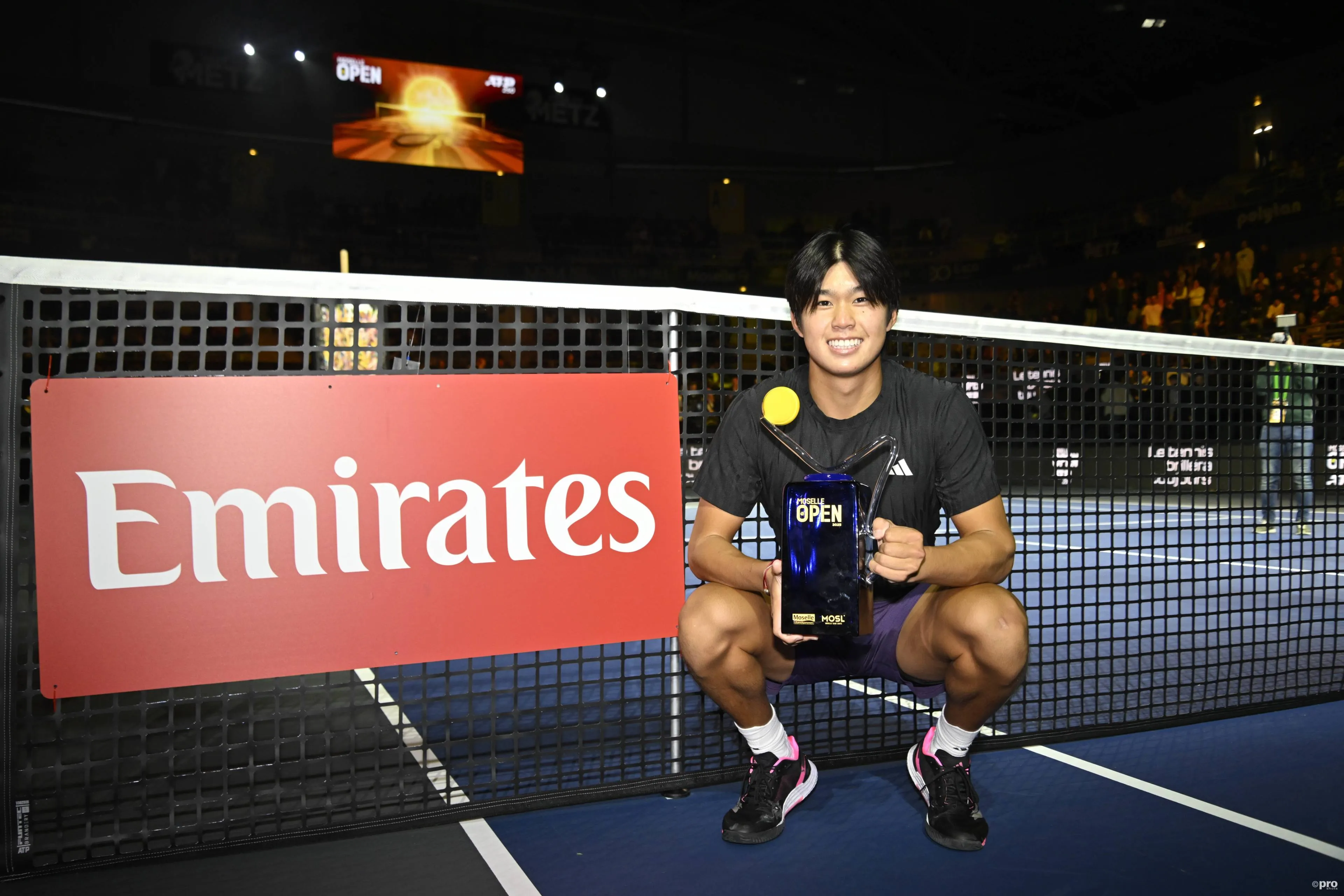 Learner Tien con el trofeo del Moselle Open en la mano delante de una red.