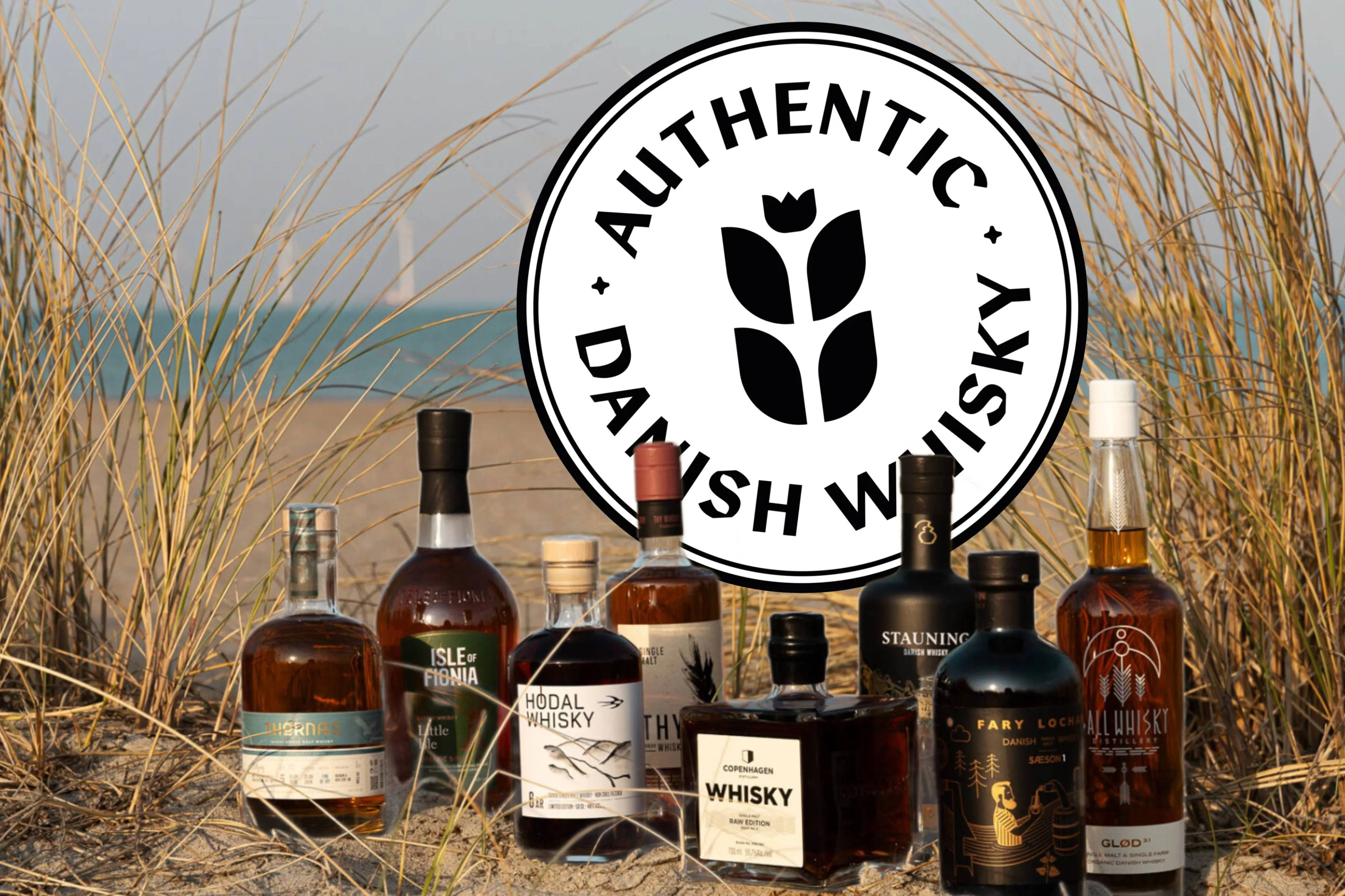 Deense whiskyflessen op een strand met duingras en het Authentic Danish Whisky logo