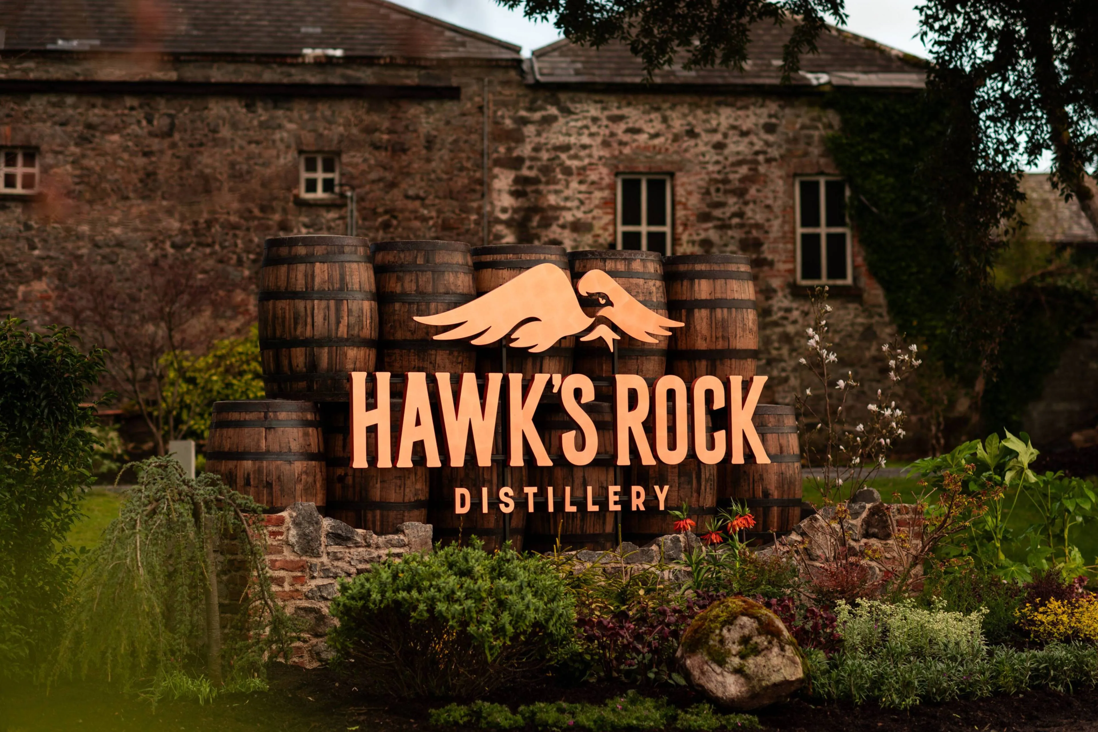 Hawks Rock distilleerderij met vaten op de voorgrond en het logo