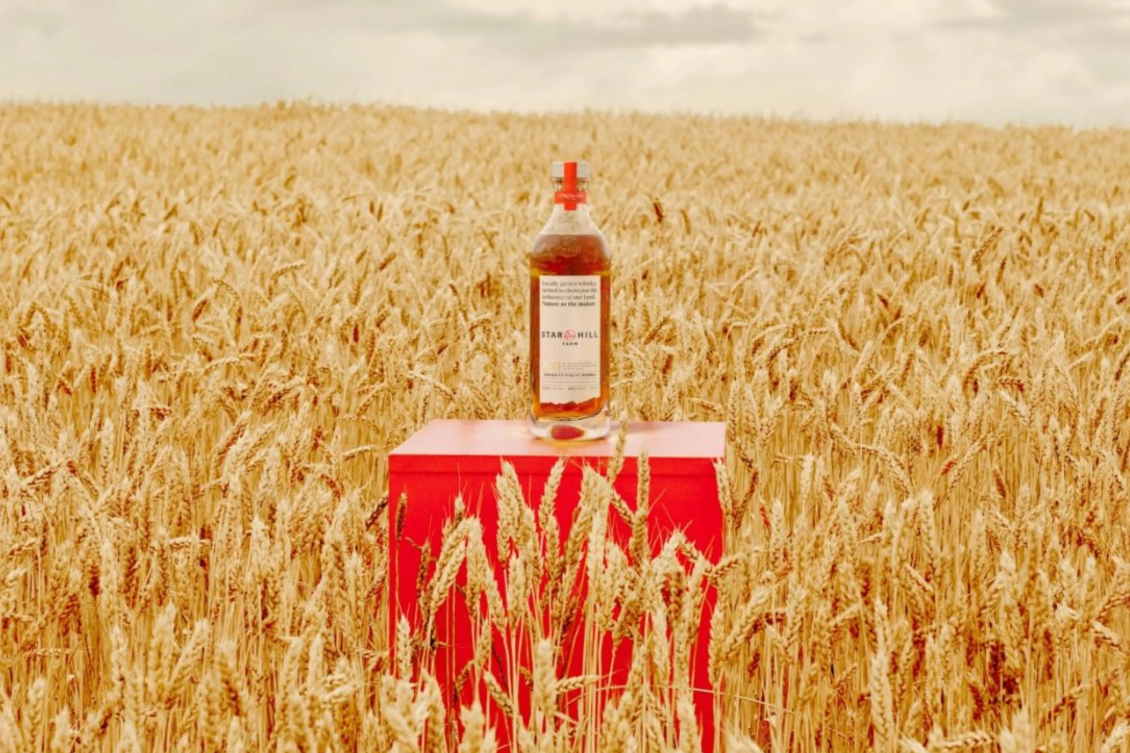 Een fles Star Hill Farm whisky midden in een graanveld op een rode kist