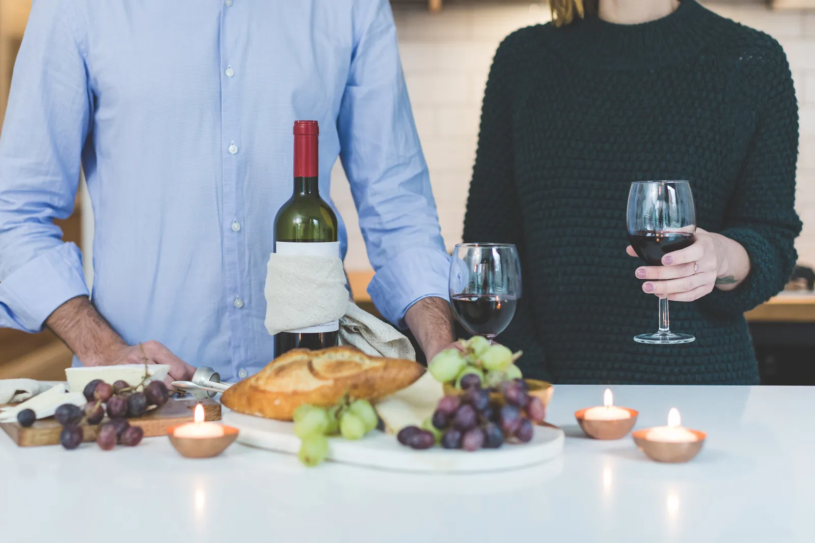 canva man standing beside woman holding wine glass in front of grapes and bread on table